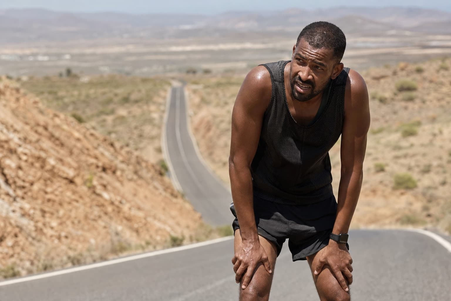 Runner climbing a hilly road in bright sun on a hot, hazy day.