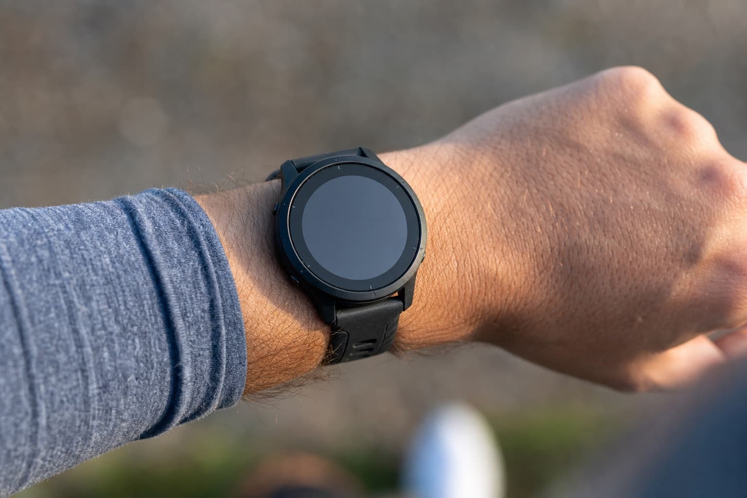 Close detail of a GPS sports watch on a runner's wrist outdoors.