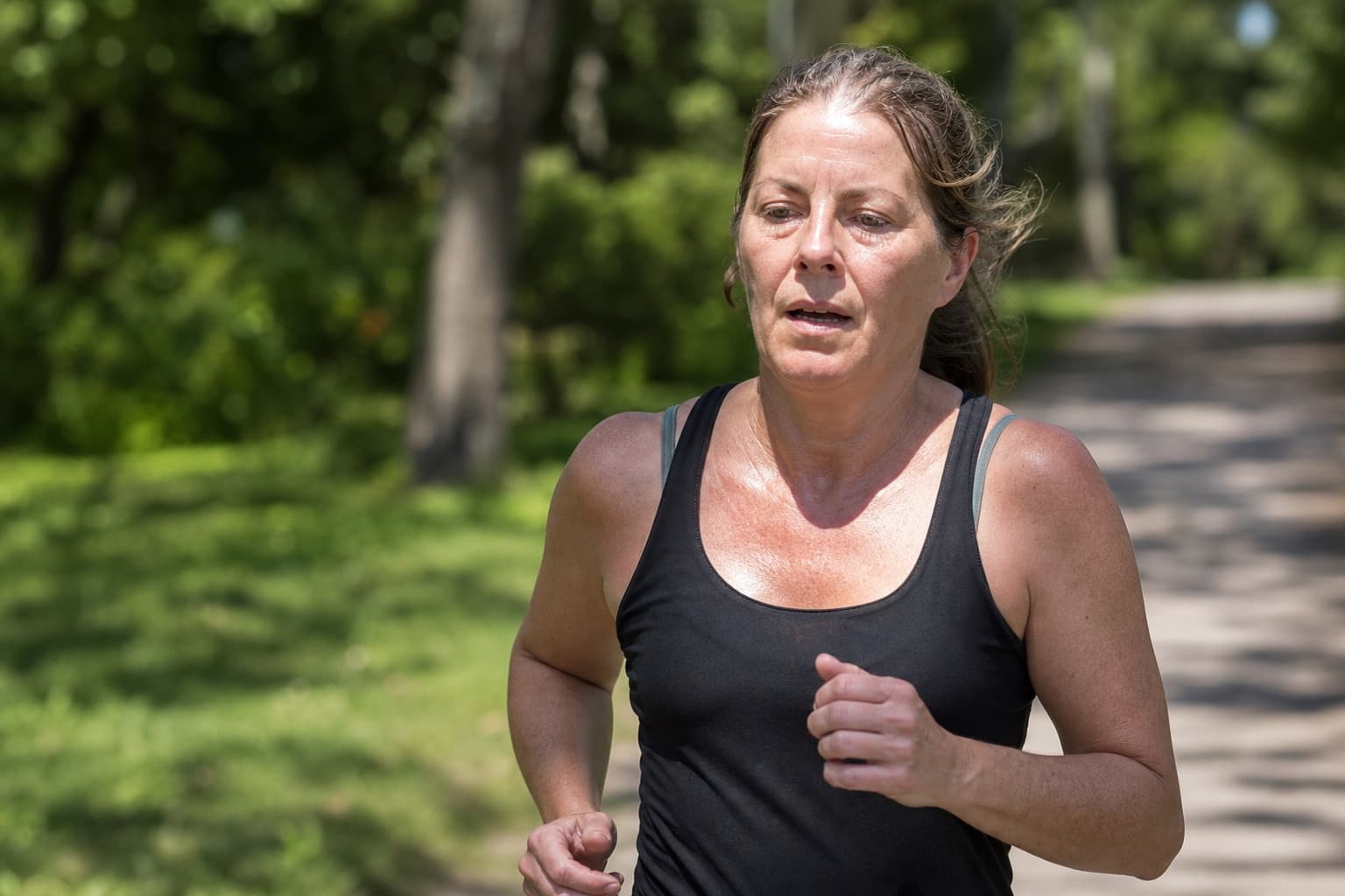 A runner in her forties pushing a hard effort on a park path.