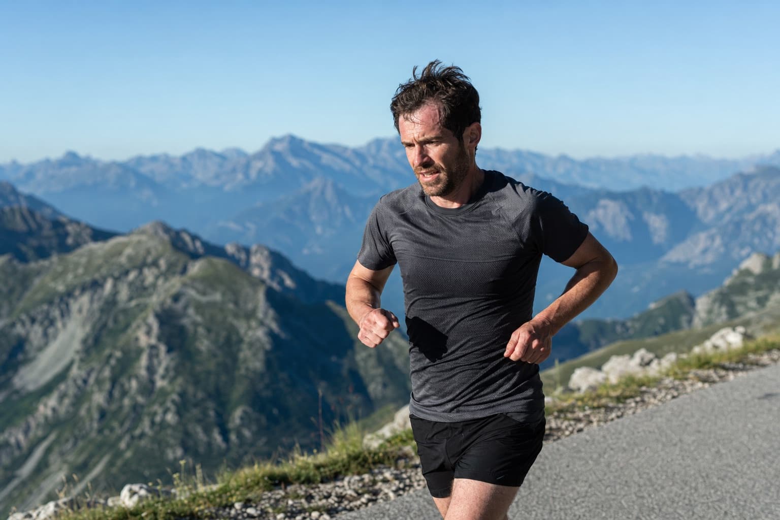 Runner racing along a mountain road with a range of peaks in the distance.