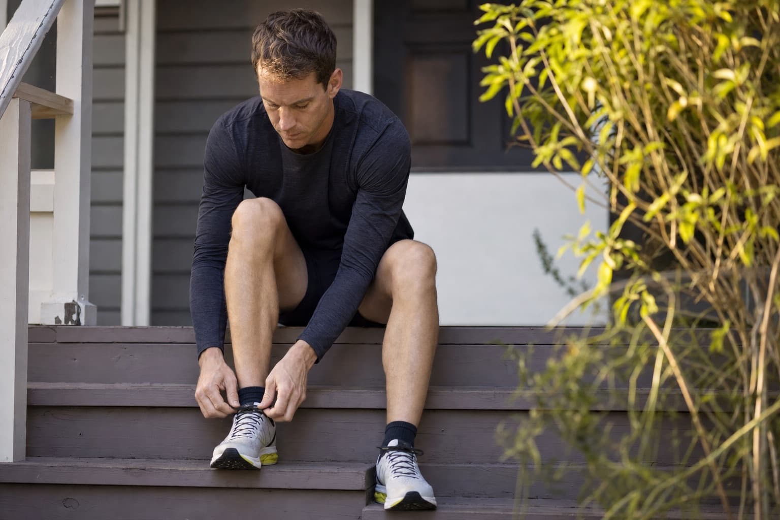 Runner lacing up running shoes on a porch before a scheduled run.