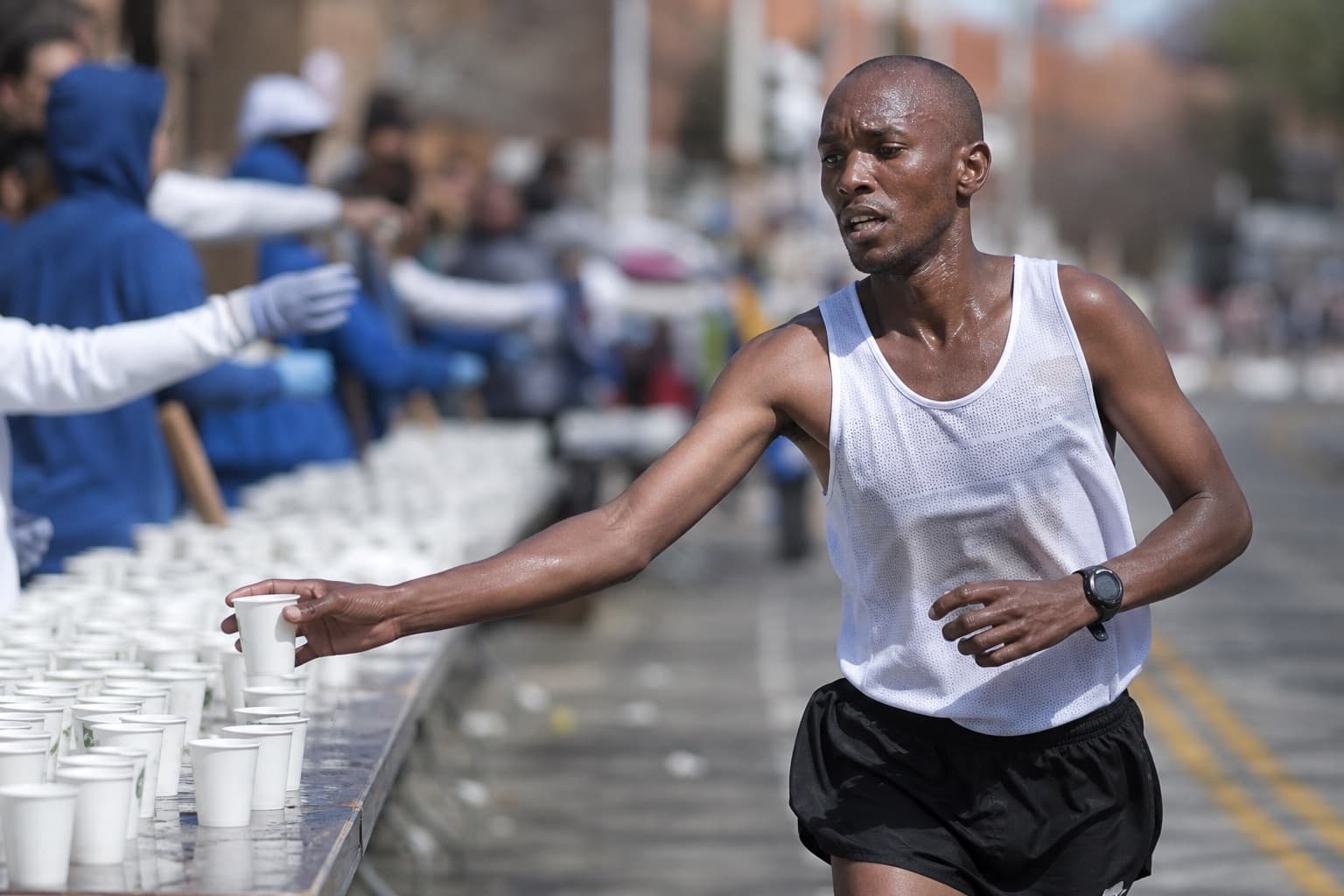 Runner grabbing a small water cup at a marathon aid station table.