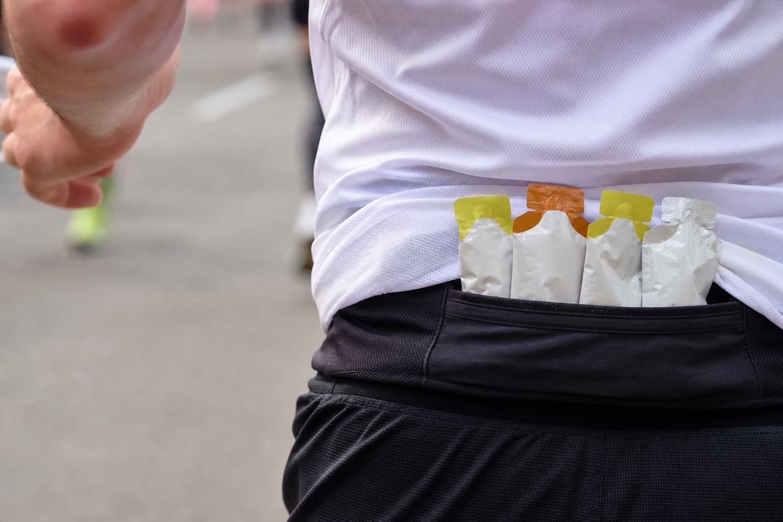 Close-up of gel packets tucked into a runner's waist belt mid-stride.