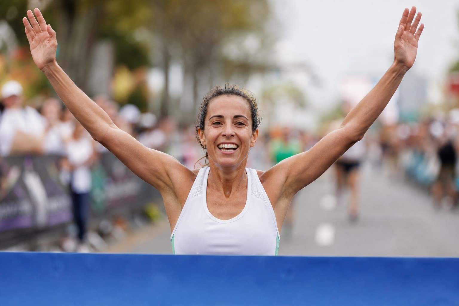 Runner crossing a race finish line with arms raised in triumph.