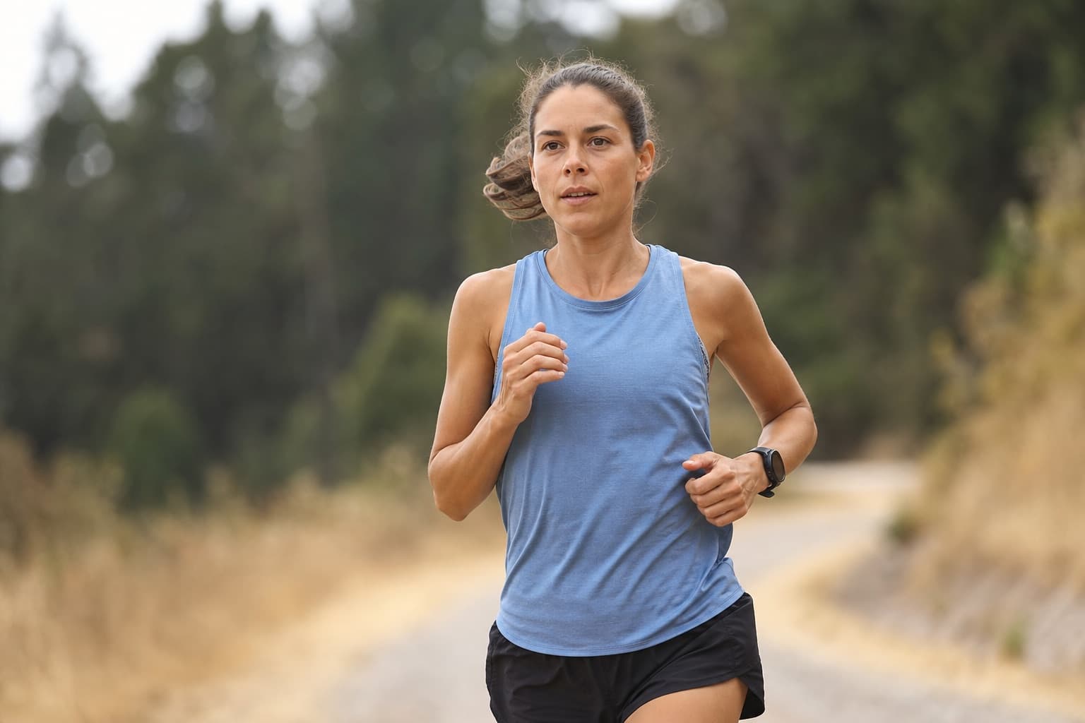 Runner wearing a GPS sports watch mid-run on an open outdoor trail.