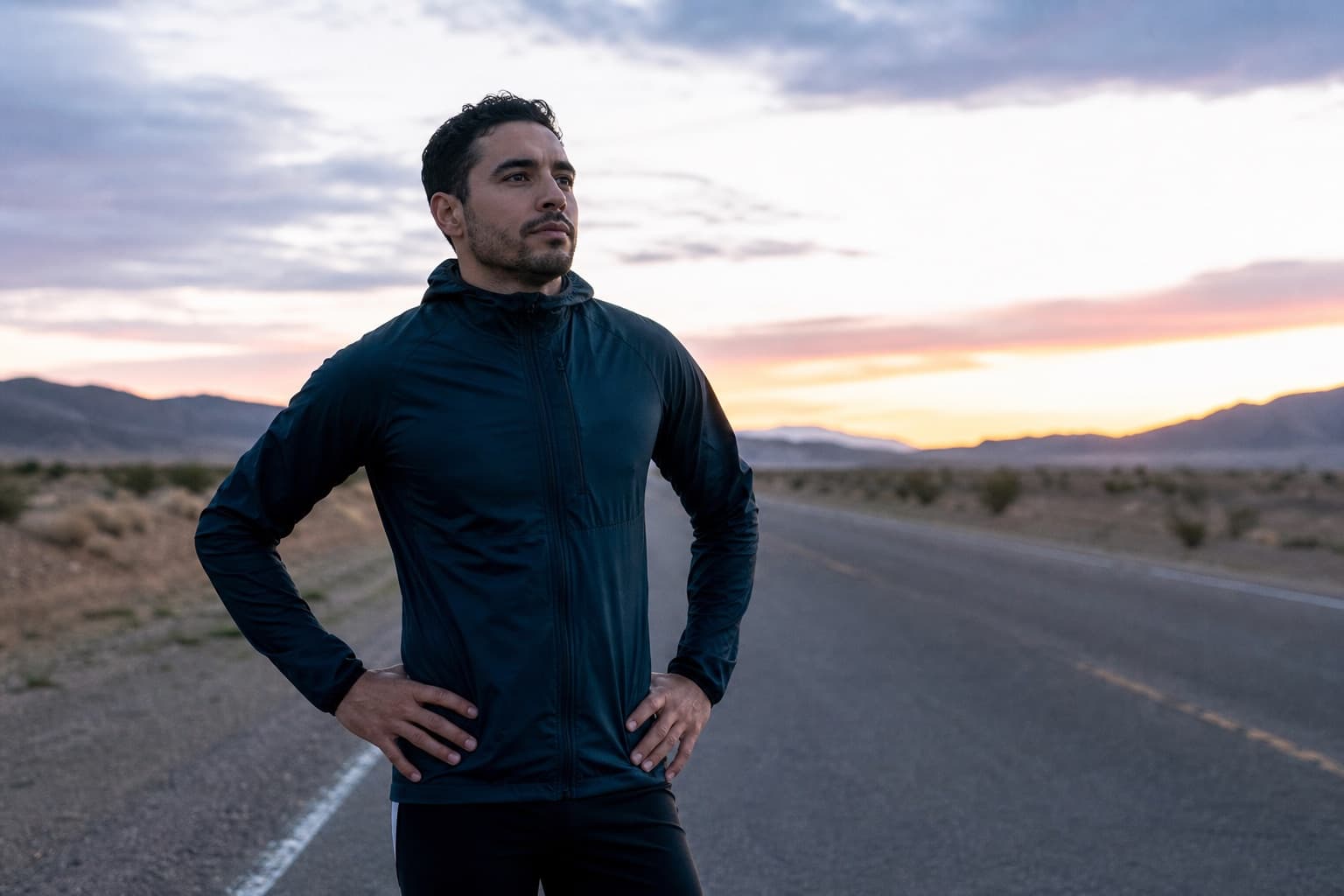 Confident runner standing composed at the start of an open road at dawn, looking ahead.