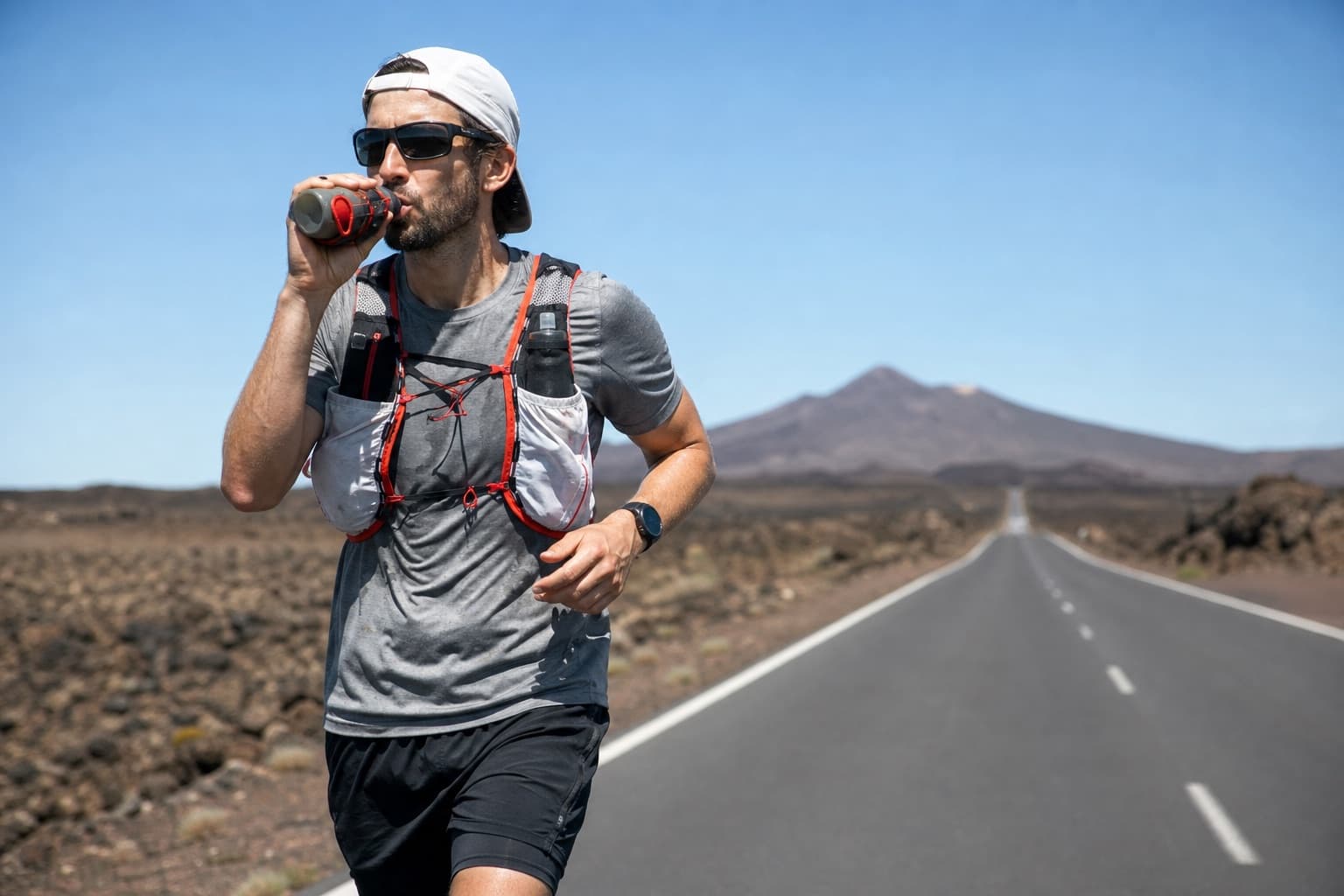 Marathon runner drinking from a handheld soft flask on an open road.