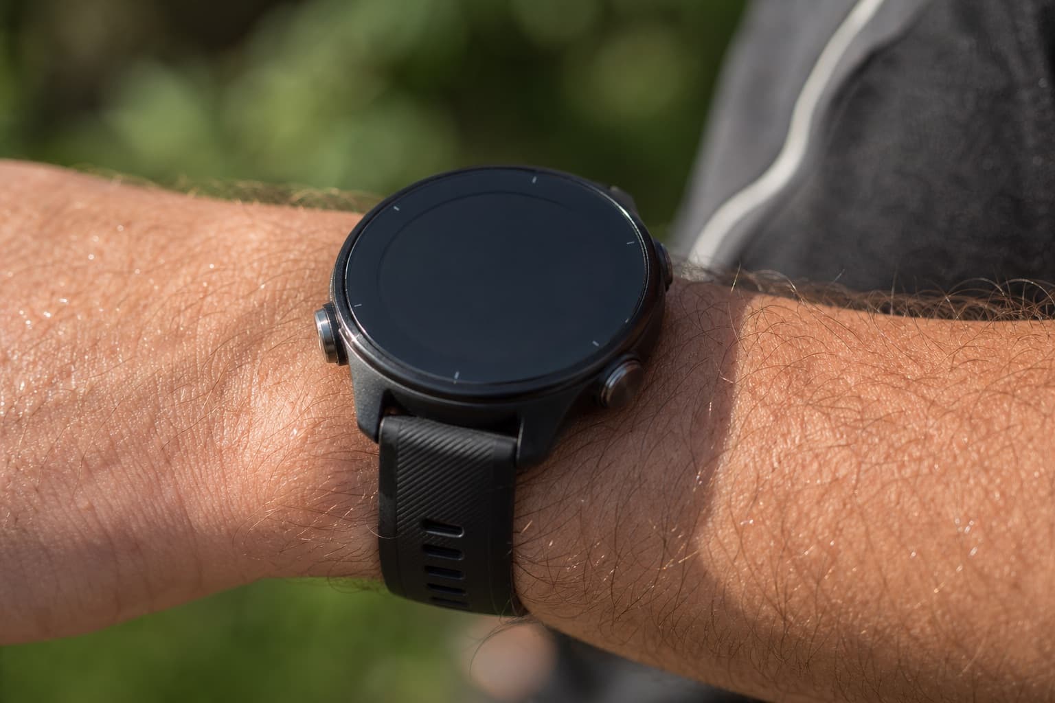 Macro view of a GPS running watch on a runner's wrist outdoors.