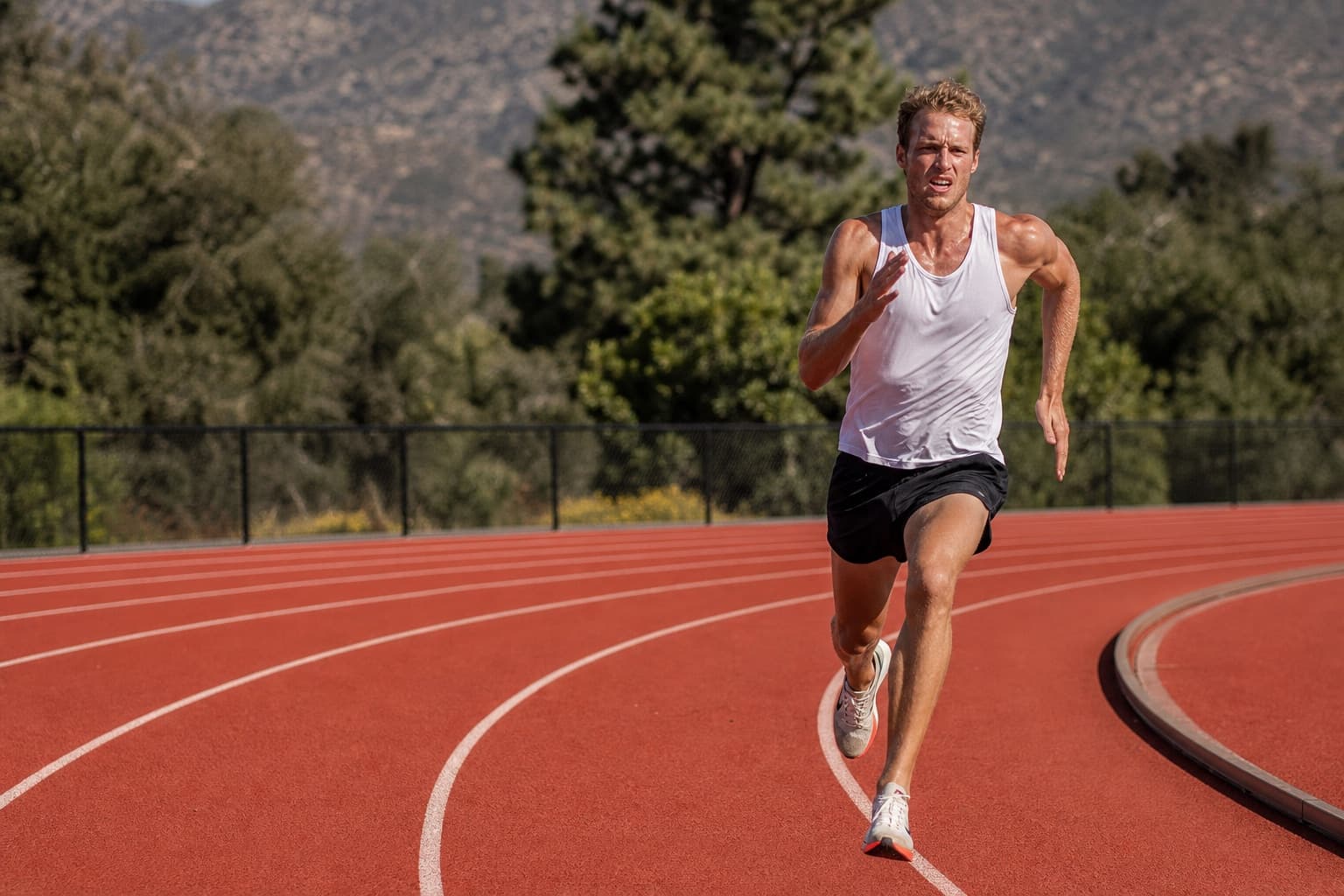 Runner in a sharp, committed interval effort on an outdoor track.