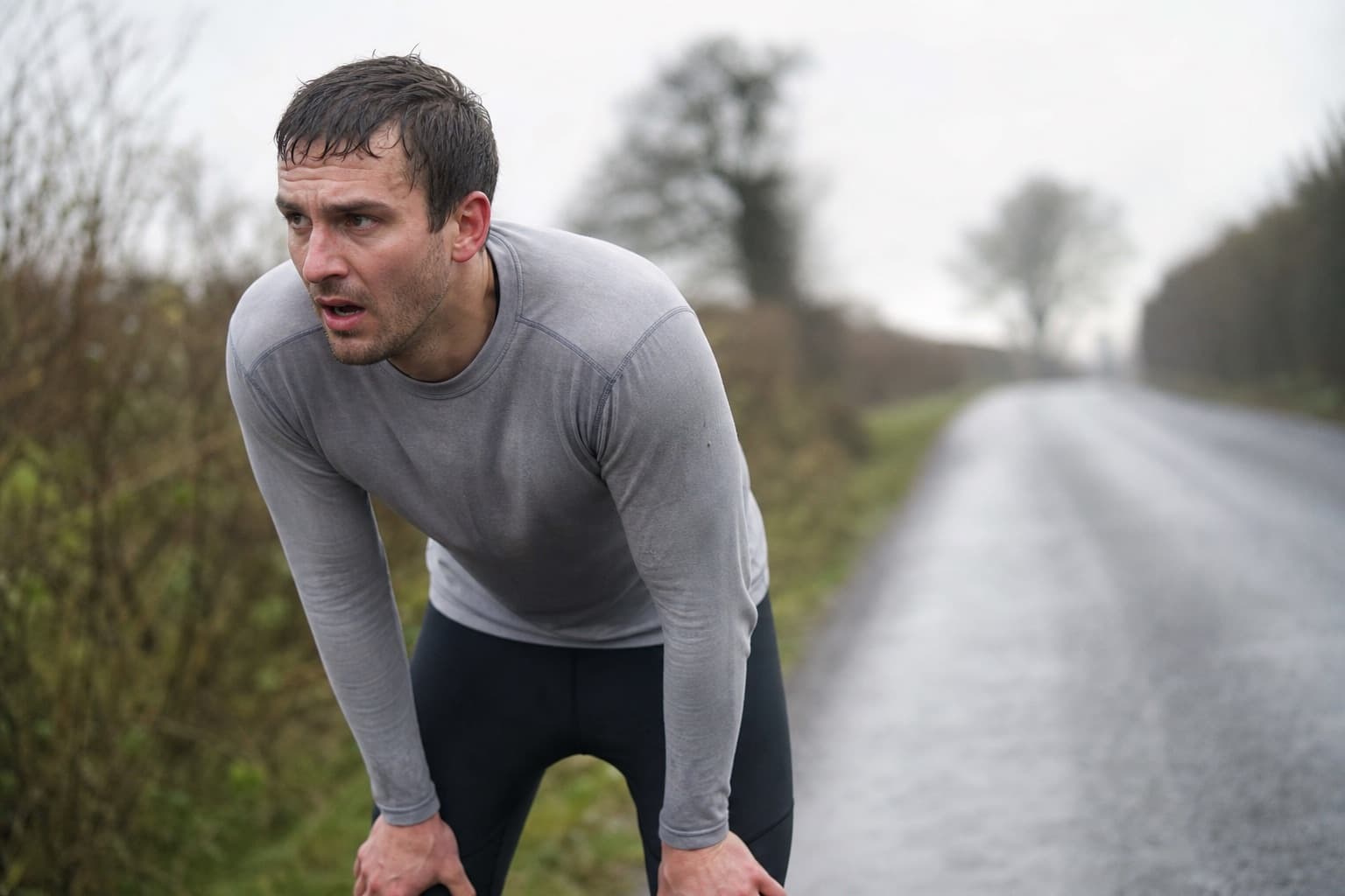 Tired runner bent with hands on knees on a road, frustrated after a flat effort.
