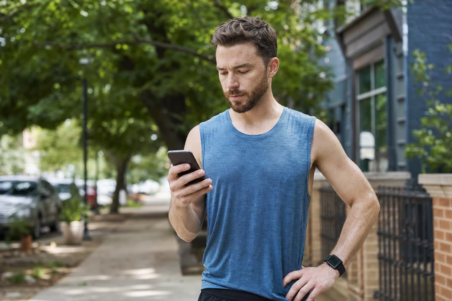 Runner on a sidewalk checking a running app on a smartphone after a workout.