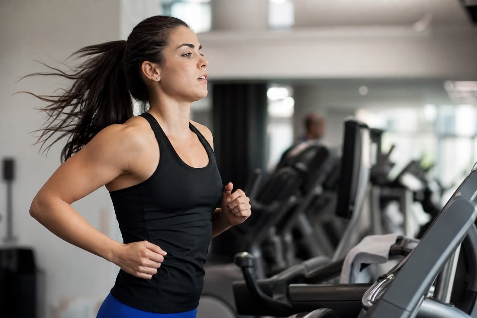 Runner holding a steady pace on a gym treadmill under bright indoor lighting.