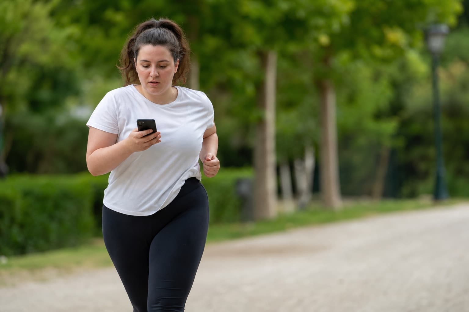 Beginner runner glancing at a phone timer during a walk-run interval.