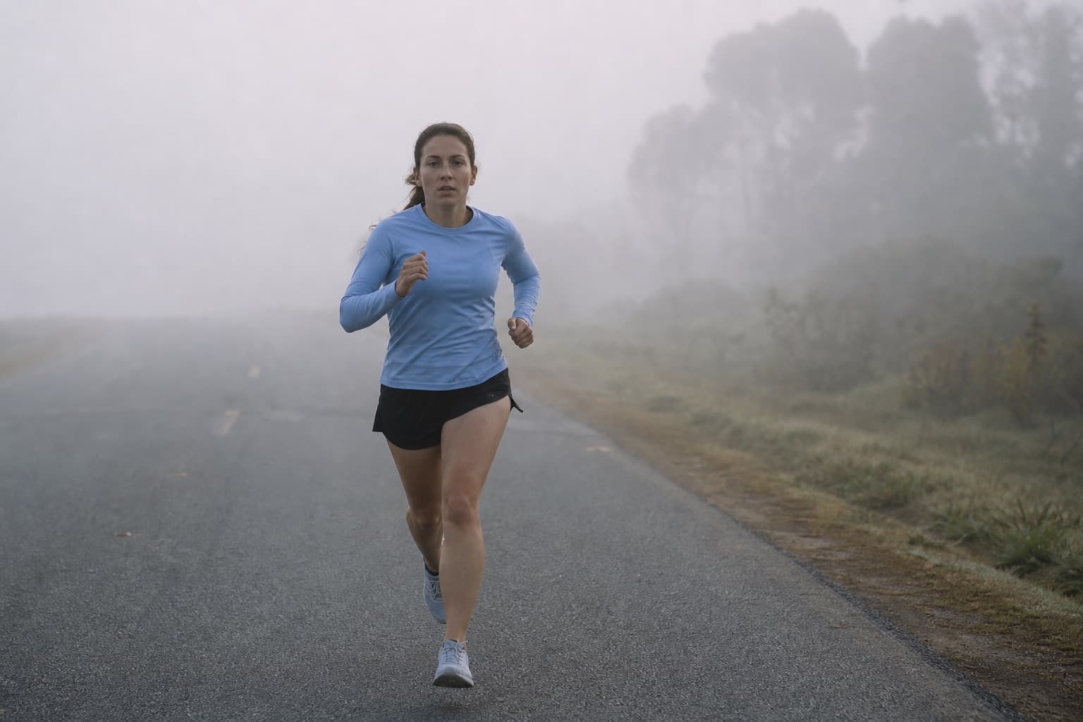 Runner disappearing into mist along a humid early-morning road.
