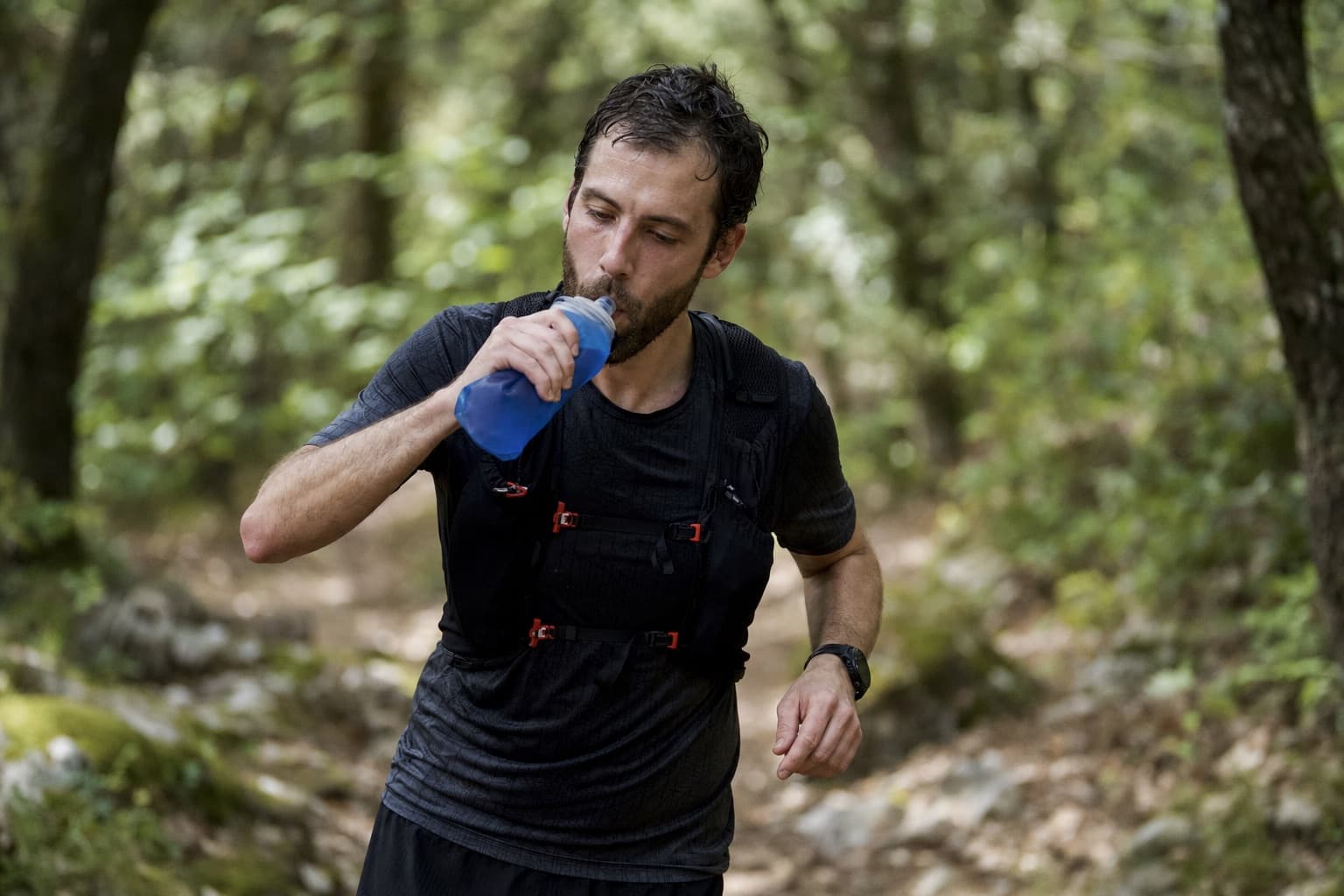 Trail runner drinking from a hydration vest during a long trail run.