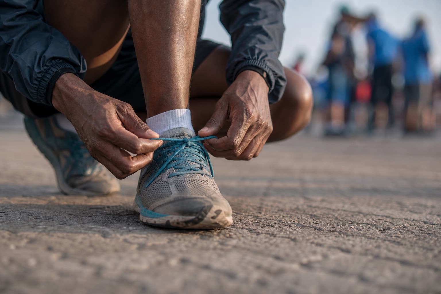 Close-up of a runner tying well-worn running shoes before a marathon.
