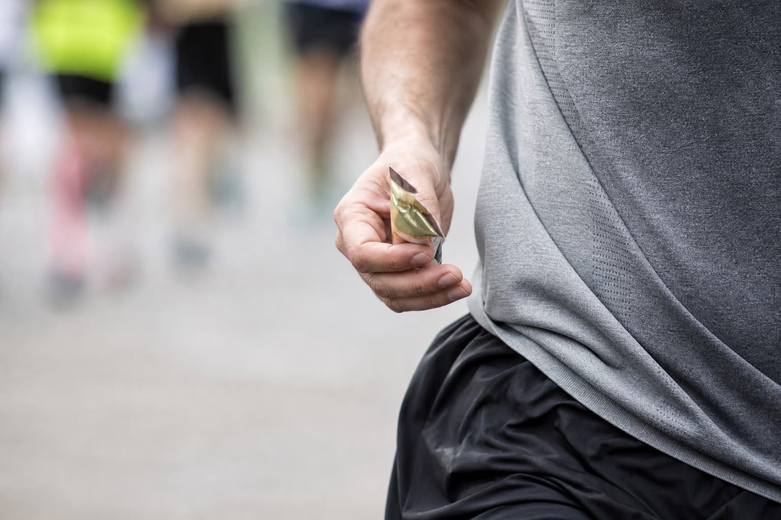 Close-up of a runner holding a single gel packet while running.