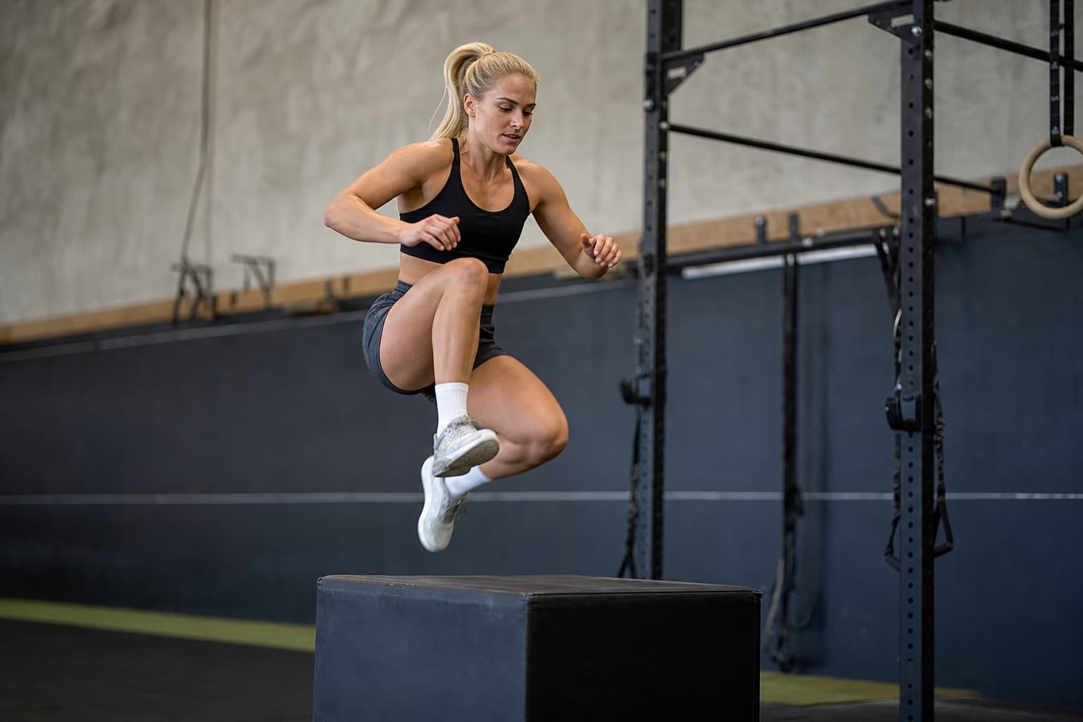 Runner performing a plyometric box jump in a gym setting.
