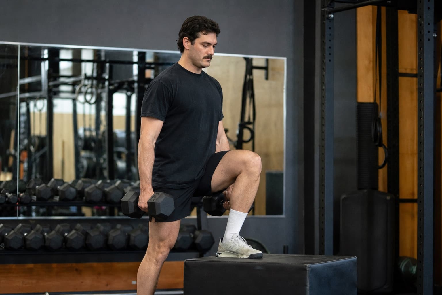 Runner performing a single-leg step-up with dumbbells in a gym.