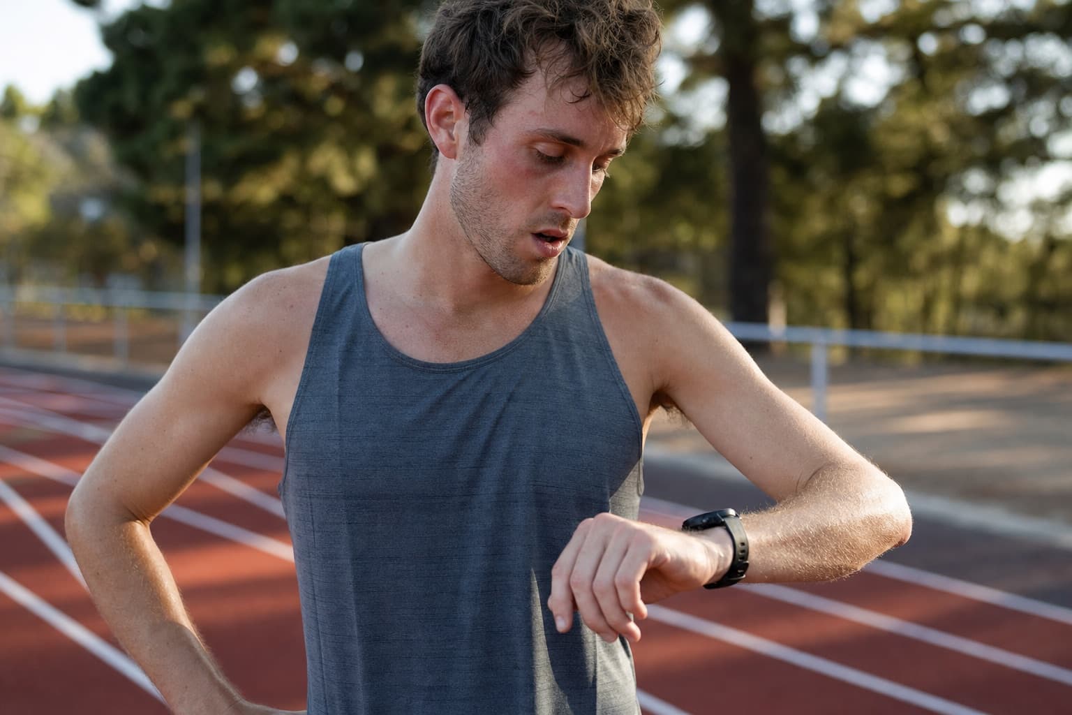 Runner glancing at a wrist watch after a fast 400-meter interval rep on a track.