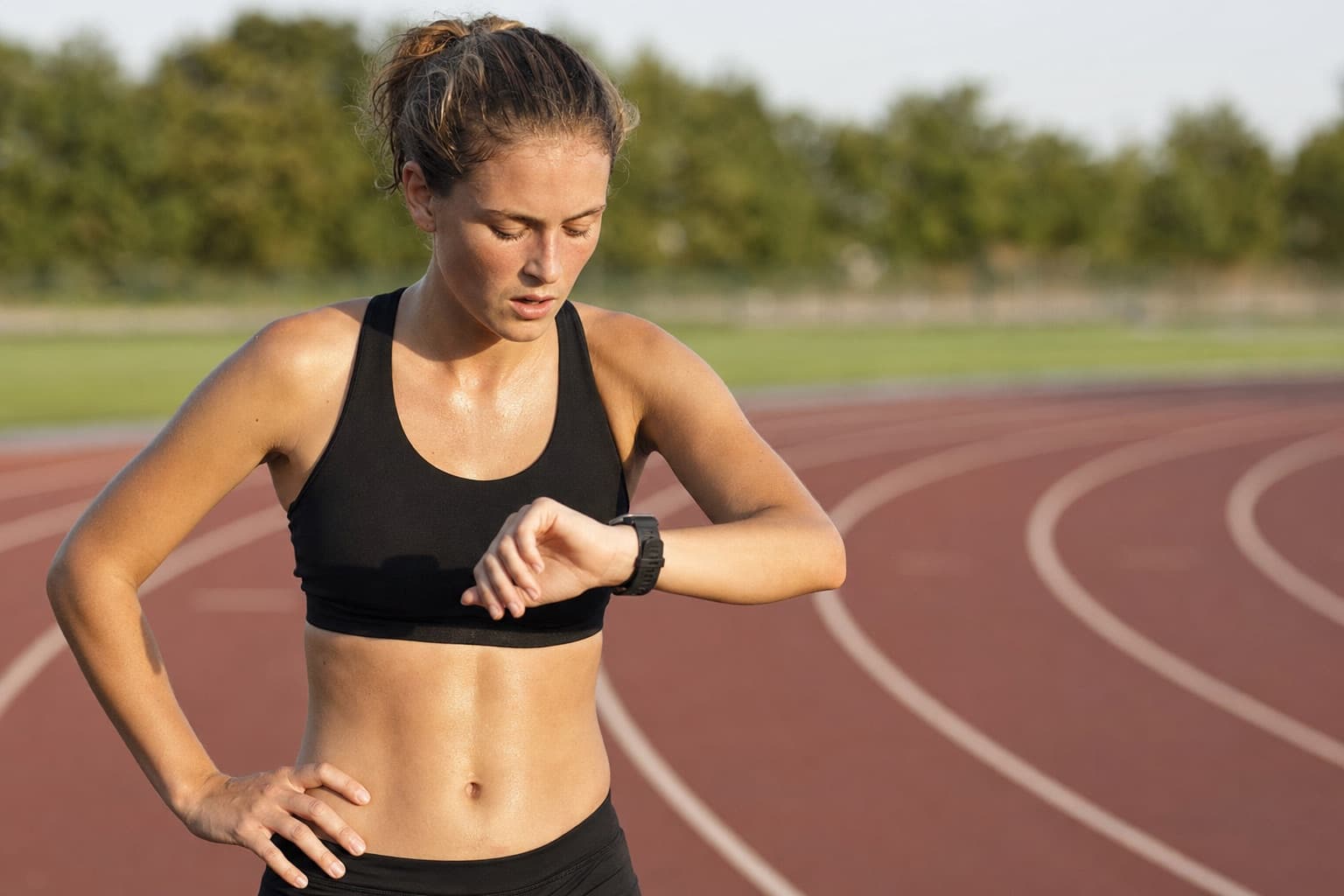 Runner checking a wrist watch between hard 800-meter interval reps on a track.