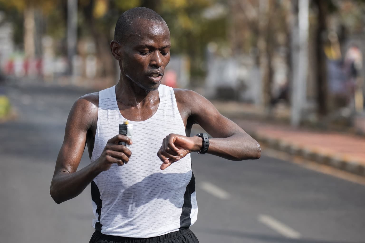 Marathon runner taking an energy gel while glancing at a wrist watch mid-race.