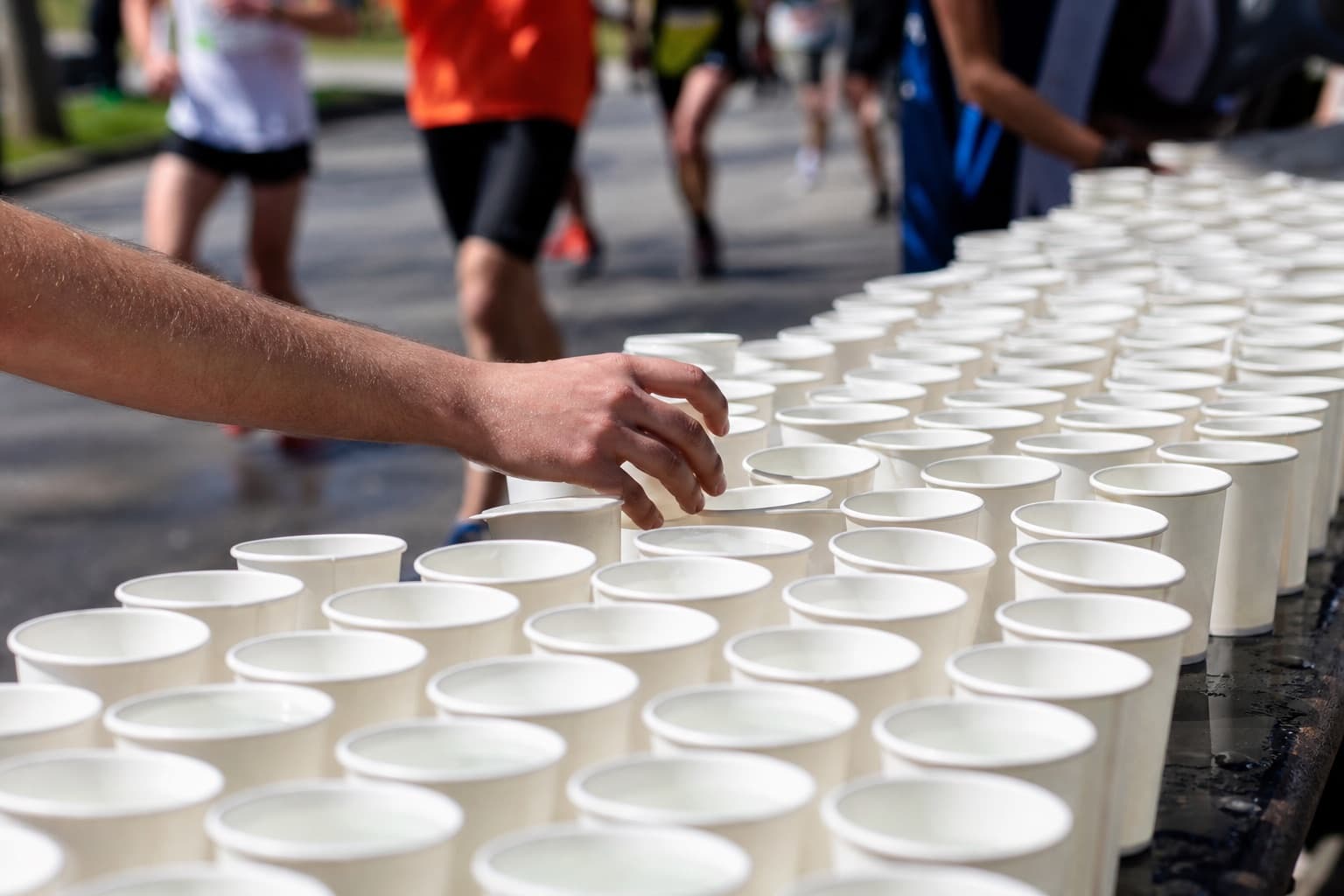 Hand reaching for a paper water cup at a crowded aid station table.