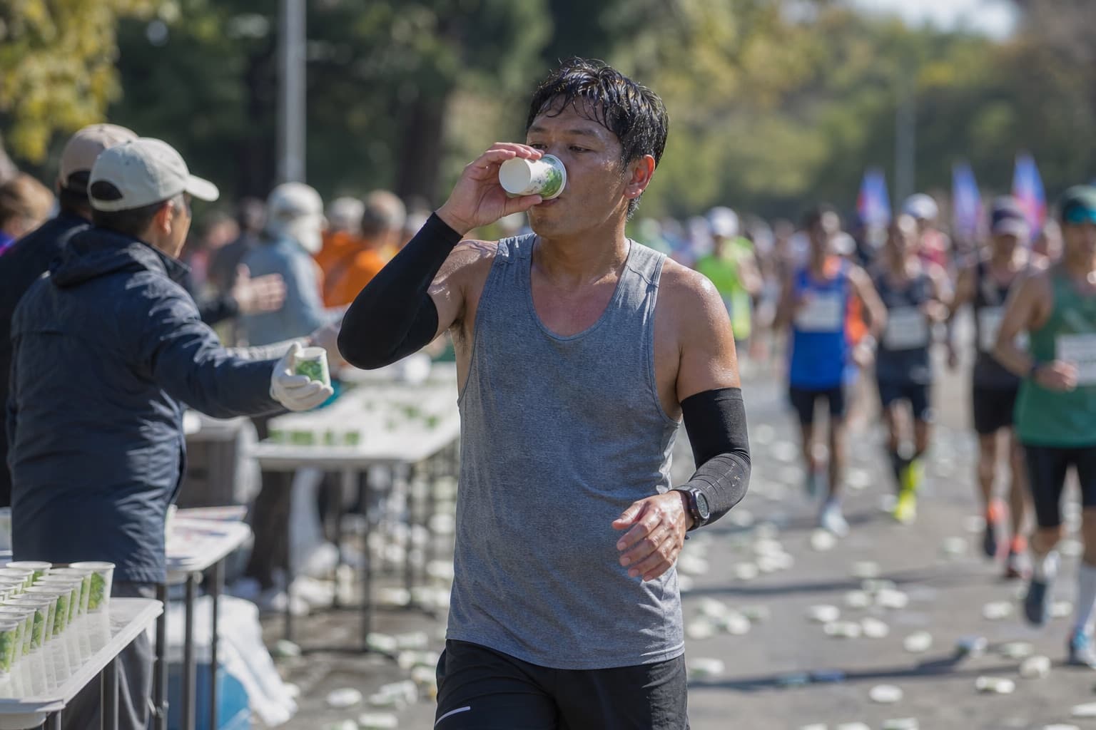 Runner drinking from a paper cup while jogging through an aid station.