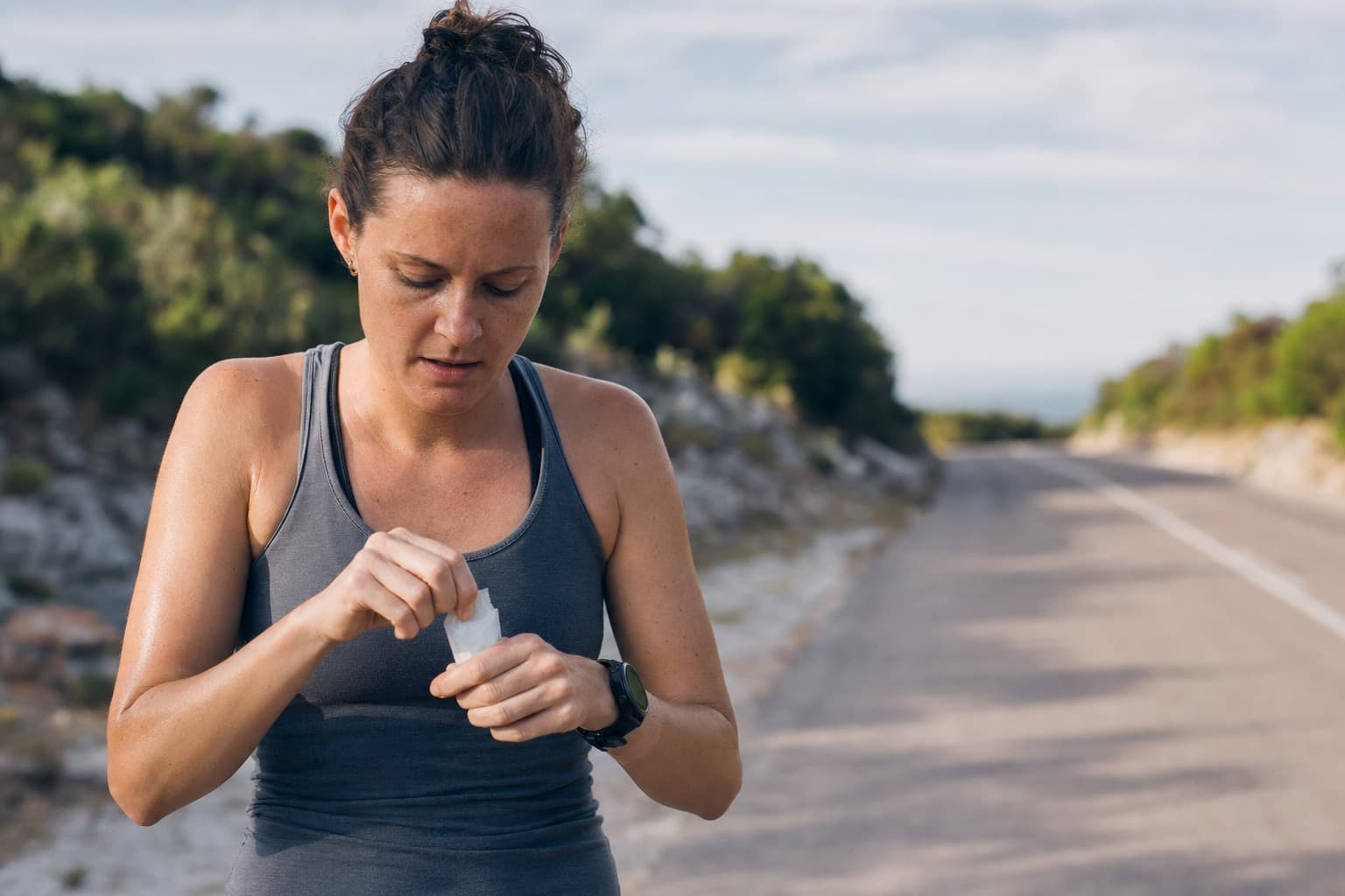 Runner taking an energy gel during a long run on a quiet road.