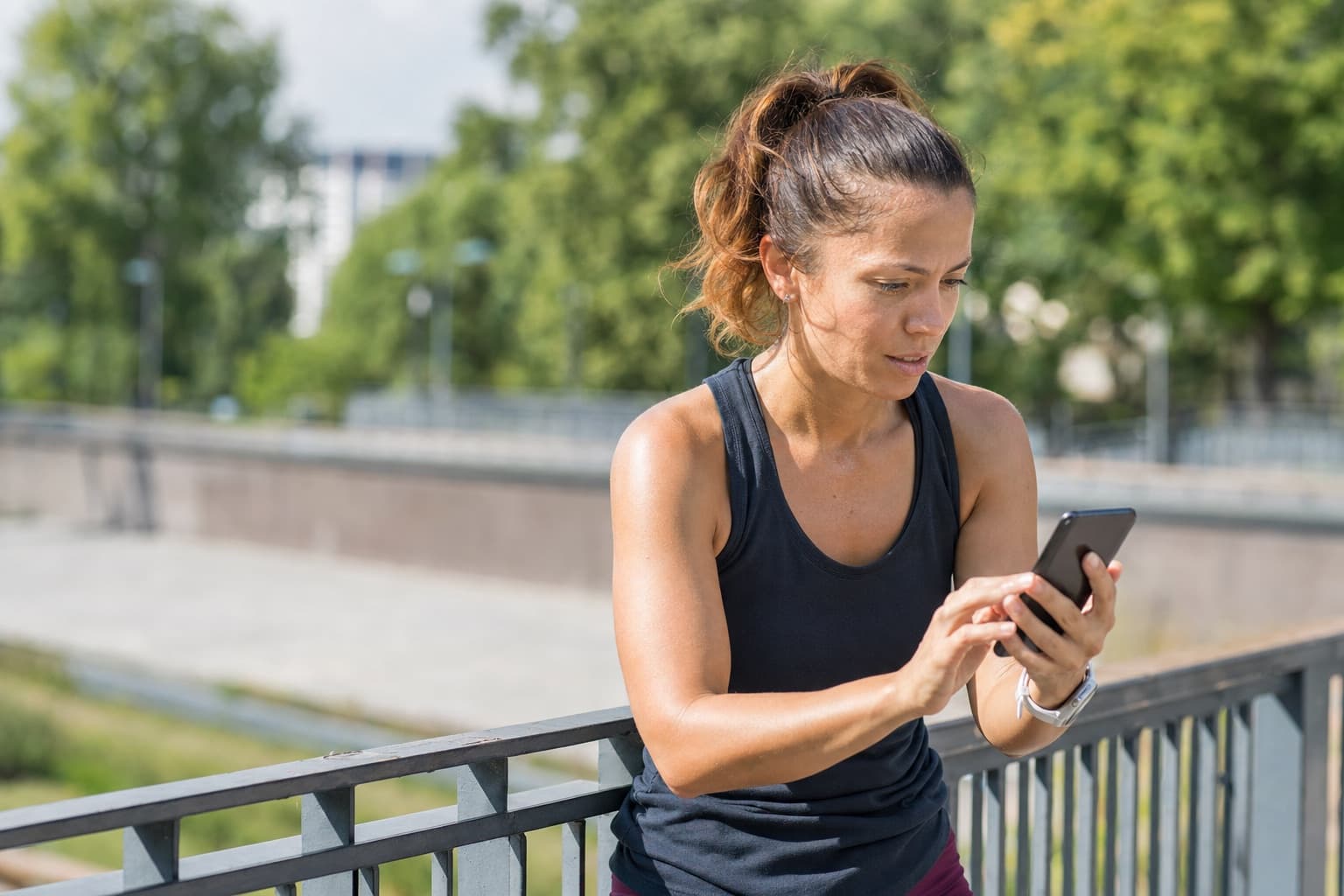 Runner reviewing training data on a phone while resting against a railing.