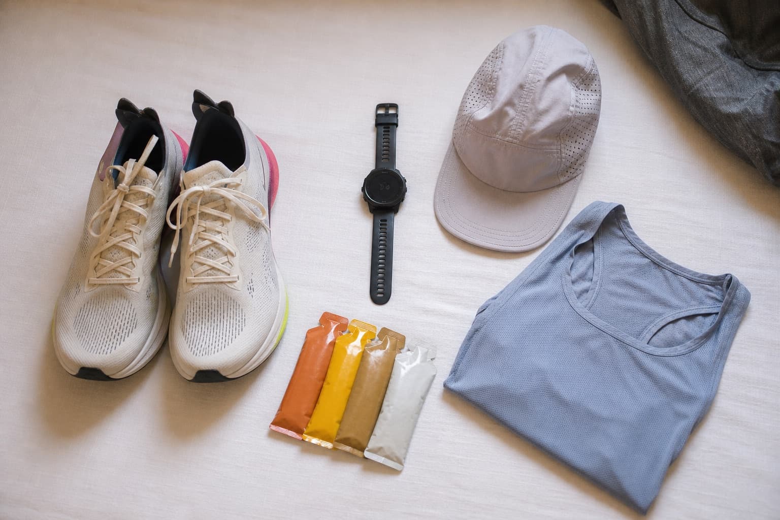Race-morning kit laid out on a bed: running shoes, GPS watch, and energy gels.