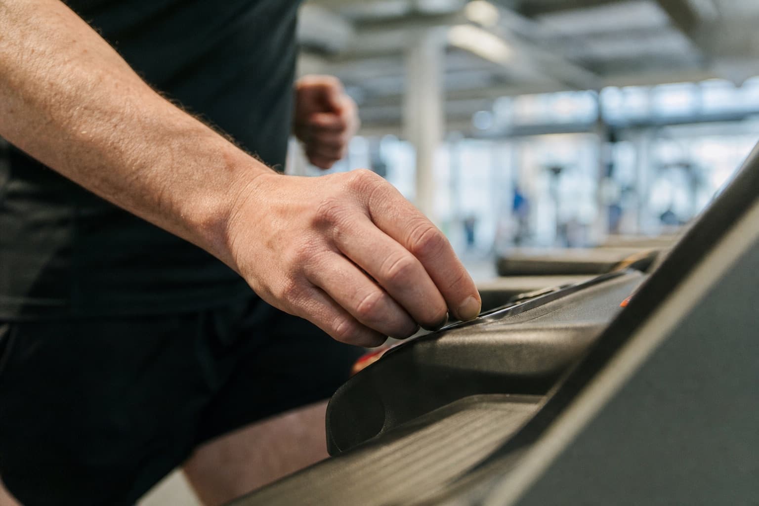 Close-up of a runner's hand adjusting the incline control on a treadmill.