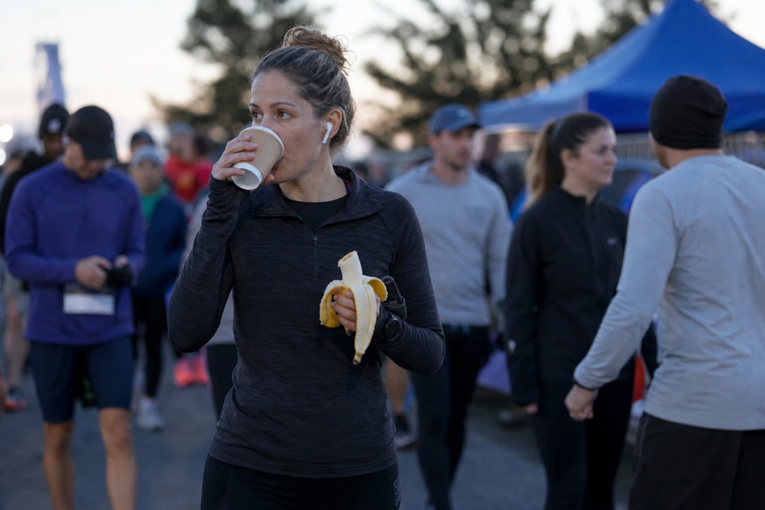 Runner sipping coffee and eating a banana while walking to the start line.