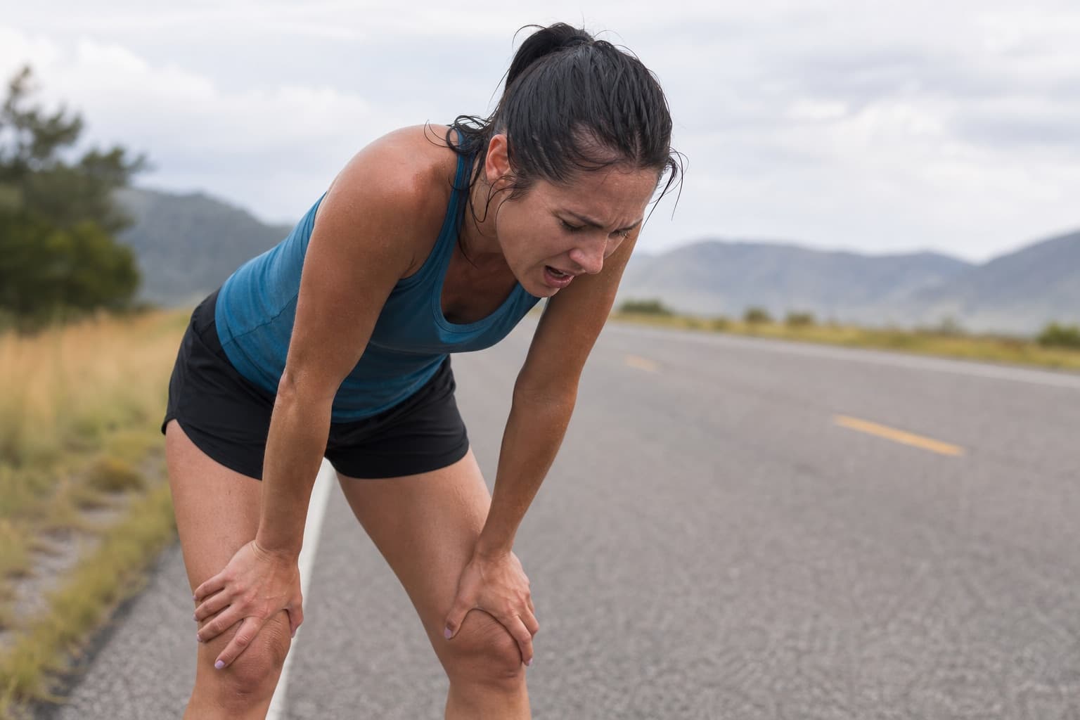 Exhausted runner bent over with hands on knees at the side of the road after fading.